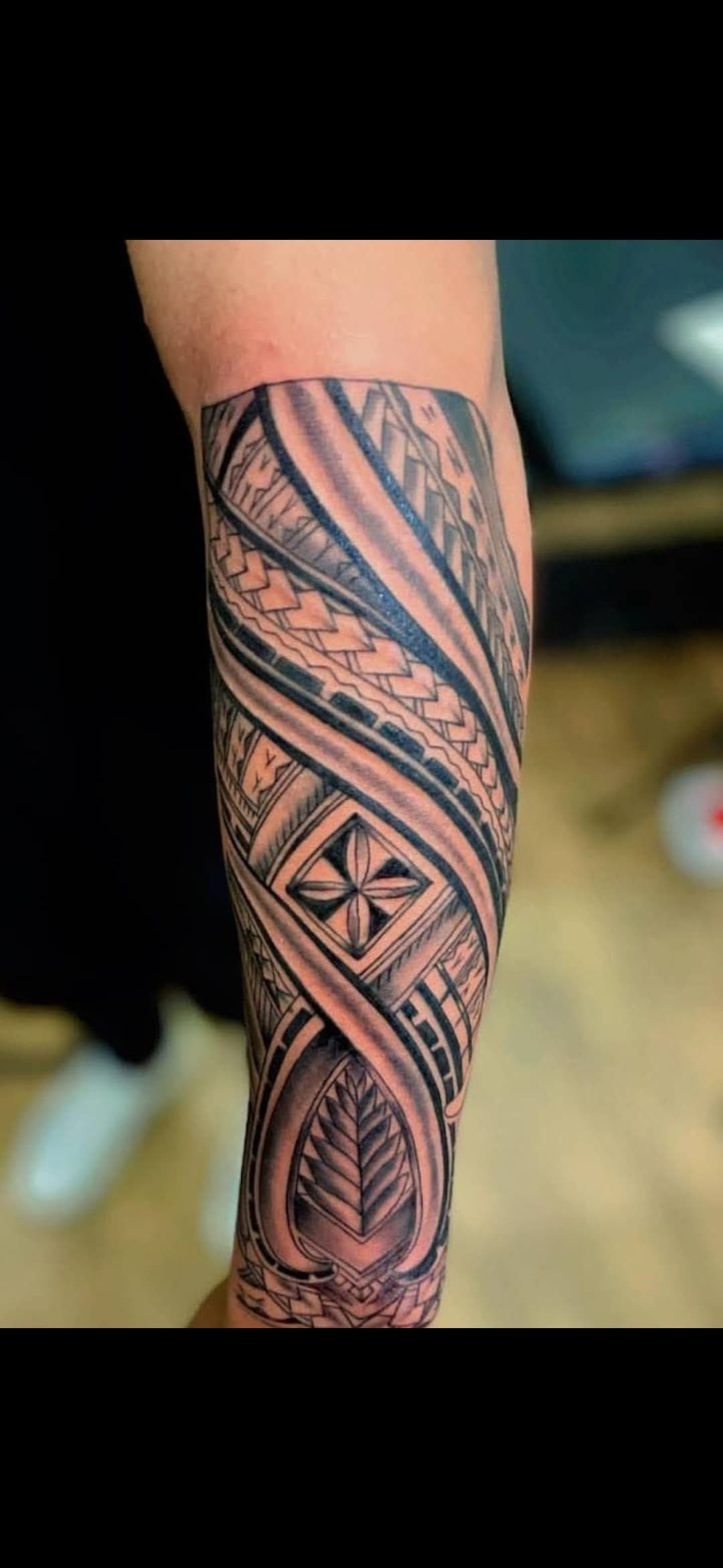 Intricate black ink tribal tattoo on a forearm featuring geometric patterns, woven bands, and leaves.
