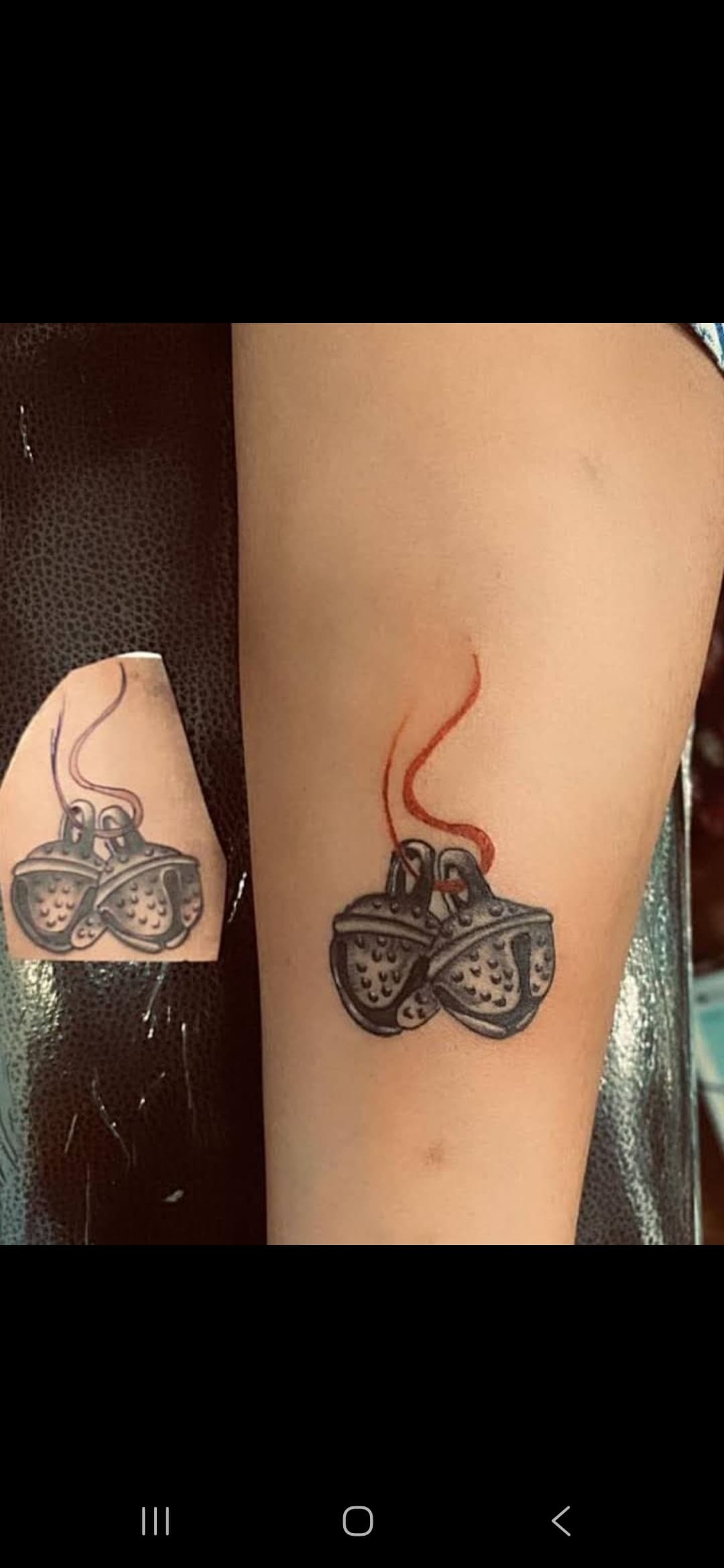 Forearm tattoo of two textured ghungroo bells tied together with a red string.