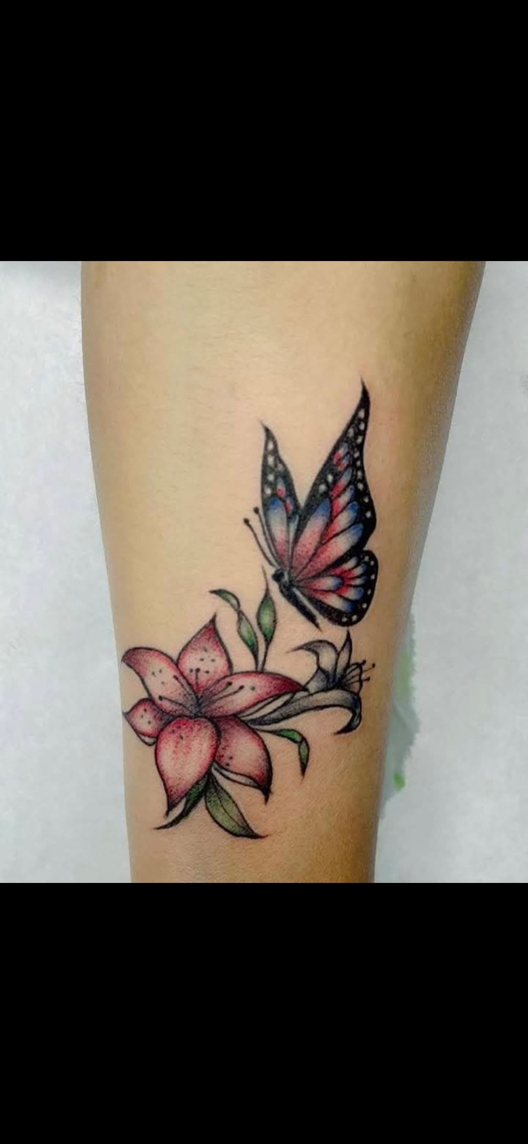 Vibrant tattoo of a pink lily and a blue and pink butterfly on a forearm.