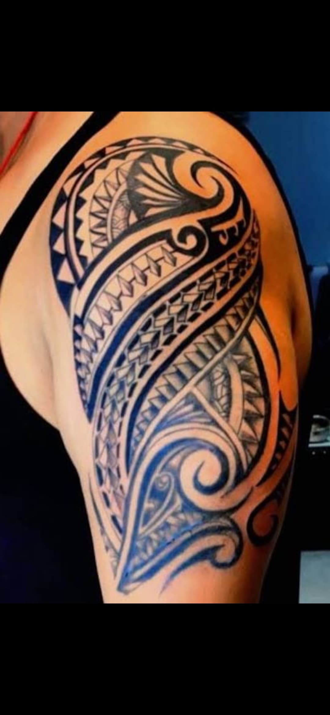 Detailed black and blue tribal tattoo with geometric patterns and swirls on a person's shoulder.