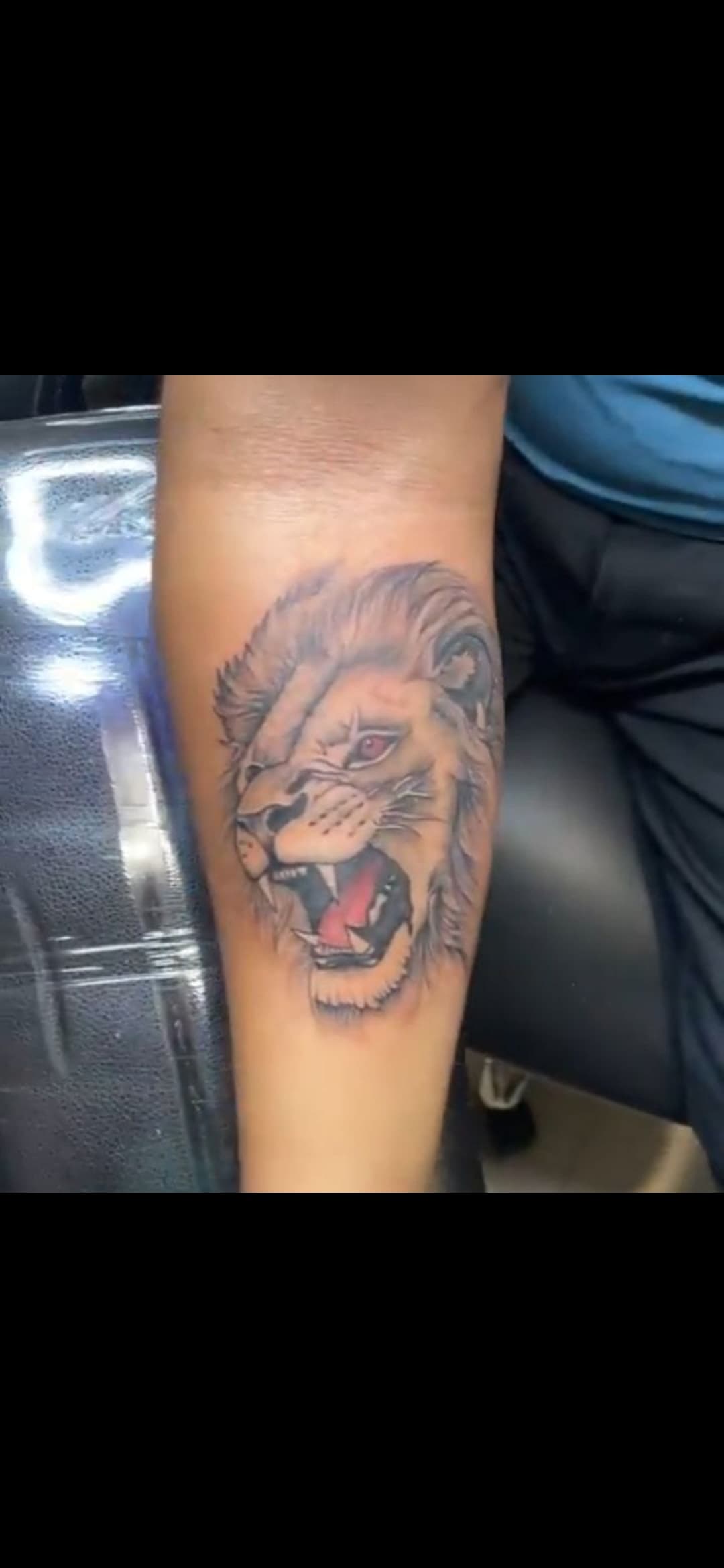 Detailed black and grey tattoo of a roaring lion with red eyes on a forearm.